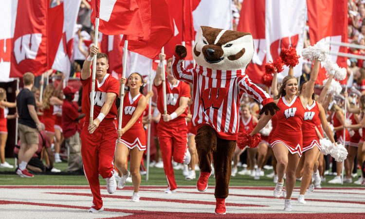 Cheerleaders and a mascot for the University of Wisconsin Badgers are clad in red and white and carrying flags during a performance at a college game in Madison, Wisconsin.