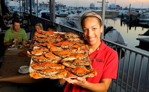 A young waitress is smiling as she displays a large tray filled with seasoned and cooked blue crabs