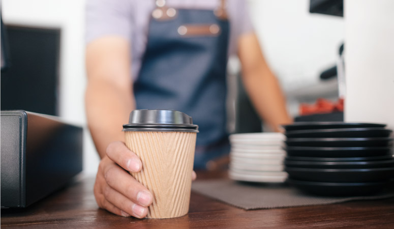 A barista is setting a to-go cup of coffee down on the counter for pick-up. 
