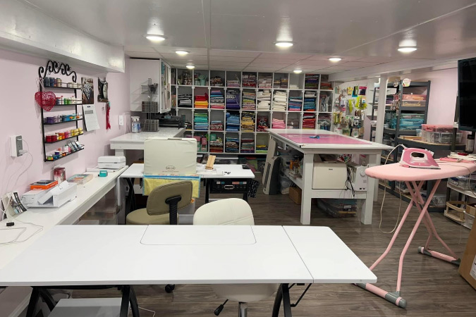A basement that has been remodeled for use as a craft room. It has built-in shelves and freestanding storage, as well as several crafting tables.