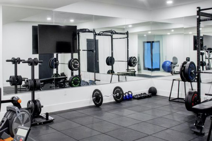 A basement that’s been transformed into a home gym, complete with mirrored walls, a mounted television, padded flooring, free weights, and exercise  machines.