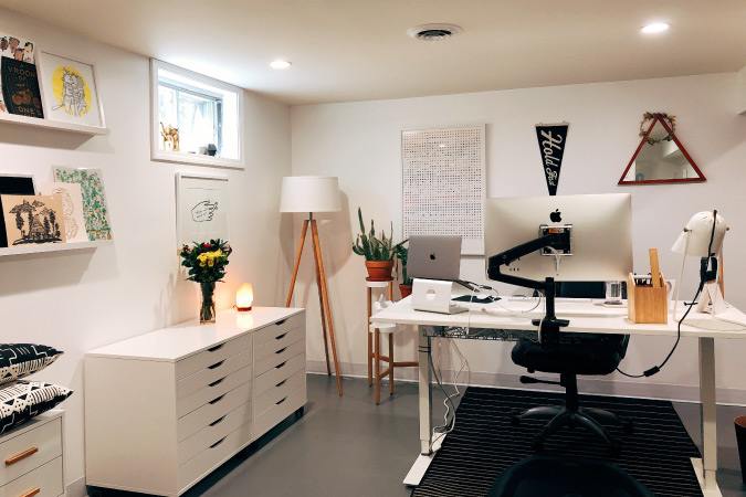 One end of a basement has been converted to a home office, with recessed lighting, office furniture, and floating shelves.