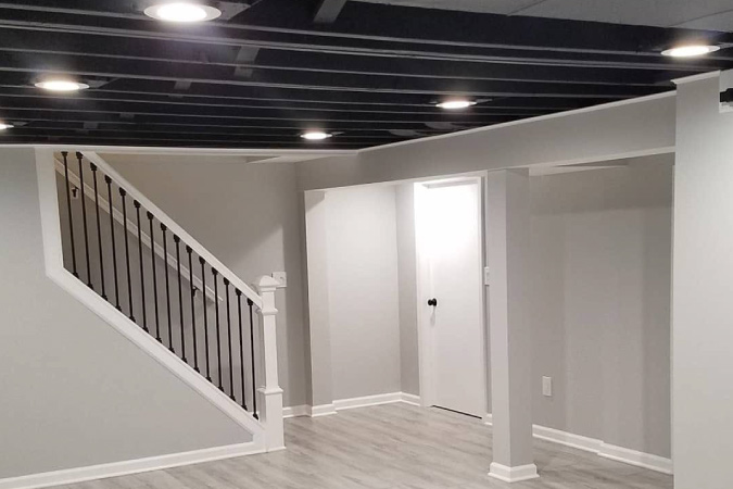 A finished basement with recessed lighting installed into the exposed basement ceiling.