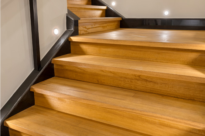 Close up of a wooden staircase leading down to the basement. There are LED lights installed low on the walls to light the steps.