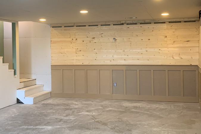 A finished basement featuring walls with a combination of wainscoting and shiplap wood.