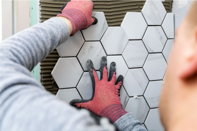 Hexagonal tiles, like the ones being installed in the picture, are just one of many bathroom remodel costs.