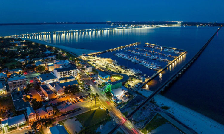 Aerial view of downtown Bay St. Louis, Mississippi, at night. The downtown features a marina and a well-lit causeway that reaches out into the water. 