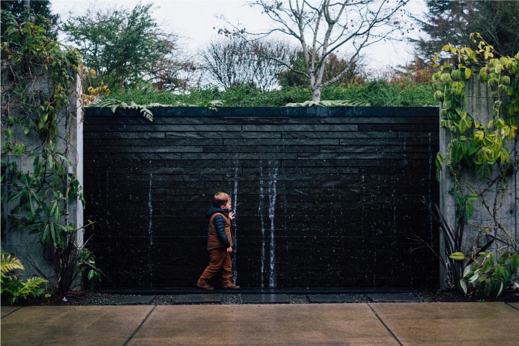 A young boy dressed in warm clothes explores a water feature at the Bellevue Botanical Garden in Bellevue, Washington.
