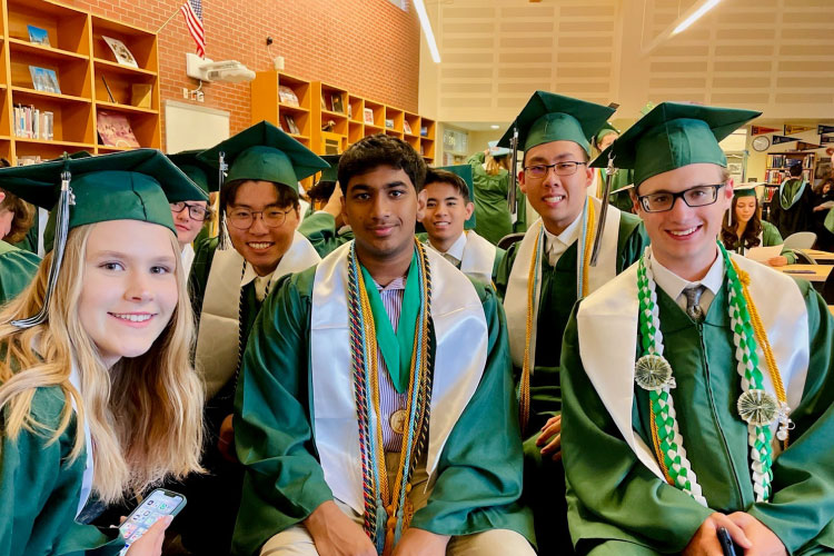 Several recent high school graduates, dressed in green caps and gowns, pose for a photo in a library in Bellevue, Washington.
