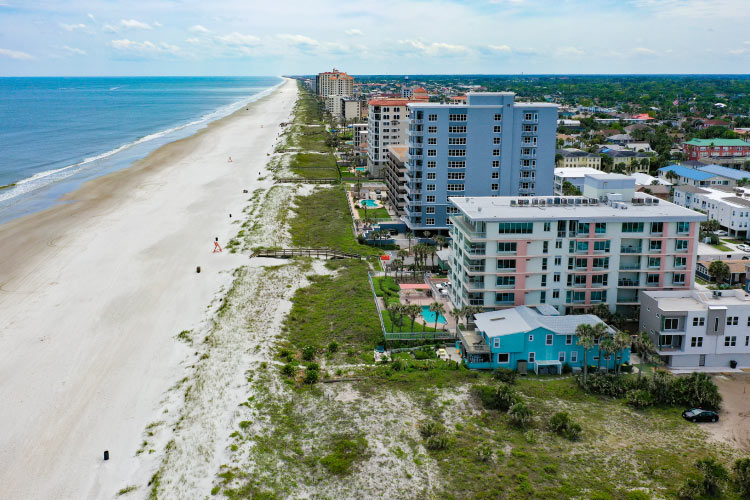 Aerial view of Jacksonville Beach in Florida on a sunny summer day. Tall pastel colored condo buildings and hotels dot the sugar-sand beaches as the calm waters lap against the coast.