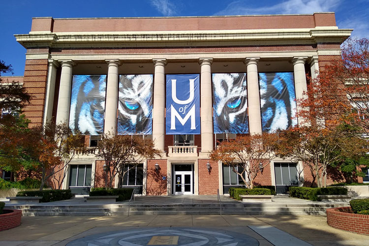 The University of Memphis Administration Building. A banner hangs behind its columns, blue with a tiger’s face. “U of M” is emblazoned on it.