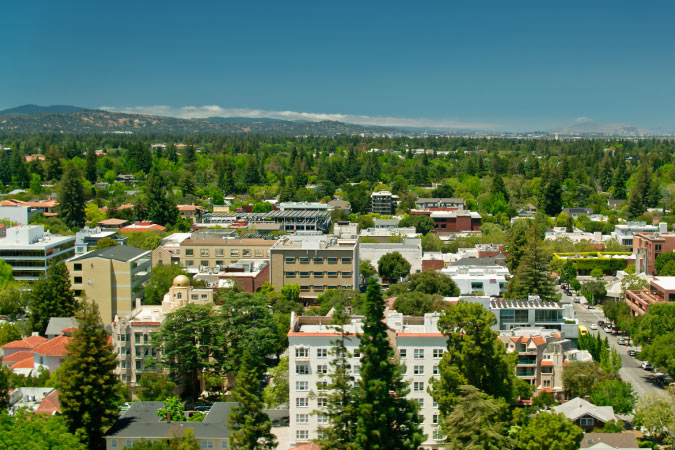 Aerial view of the lush, green city of Palo Alto, California, with the mountains visible in the distance. 