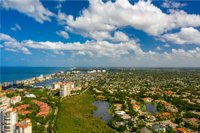 Aerial view of coastal neighborhoods in Naples, Florida, as fluffy white clouds pass overhead.