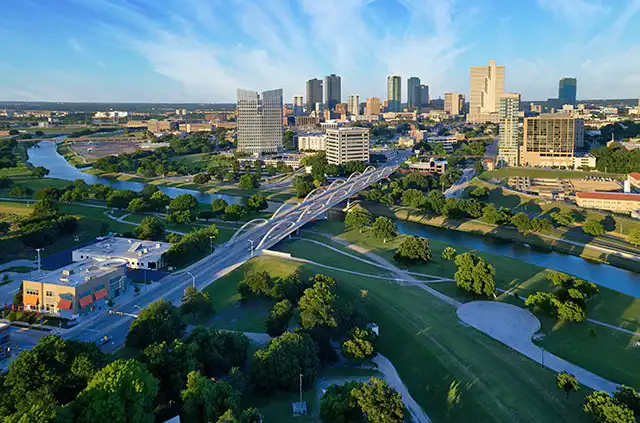 The skyline of Fort Worth, Texas. It is an aerial shot with a long bridge leading to the city with high-rise buildings.