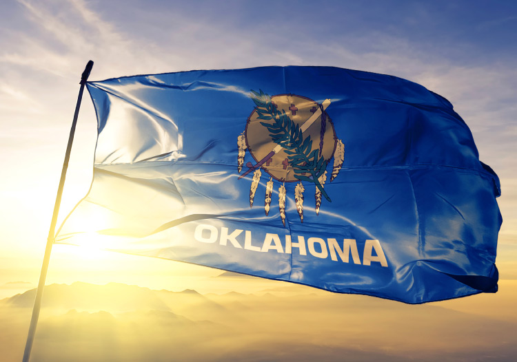 The Oklahoma state flag is blowing in the wind at the top of a simple flagpole.