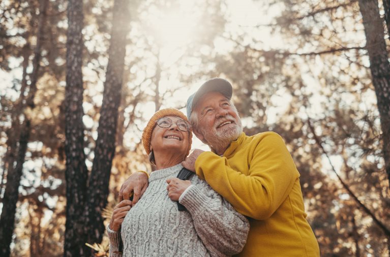 A happy retired couple is pausing during a hike through the woods to admire the beautiful surroundings. 