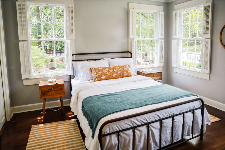 A small bedroom is spruced up with pops of color in the bedding, a unique bedframe, and textured floor rugs. 