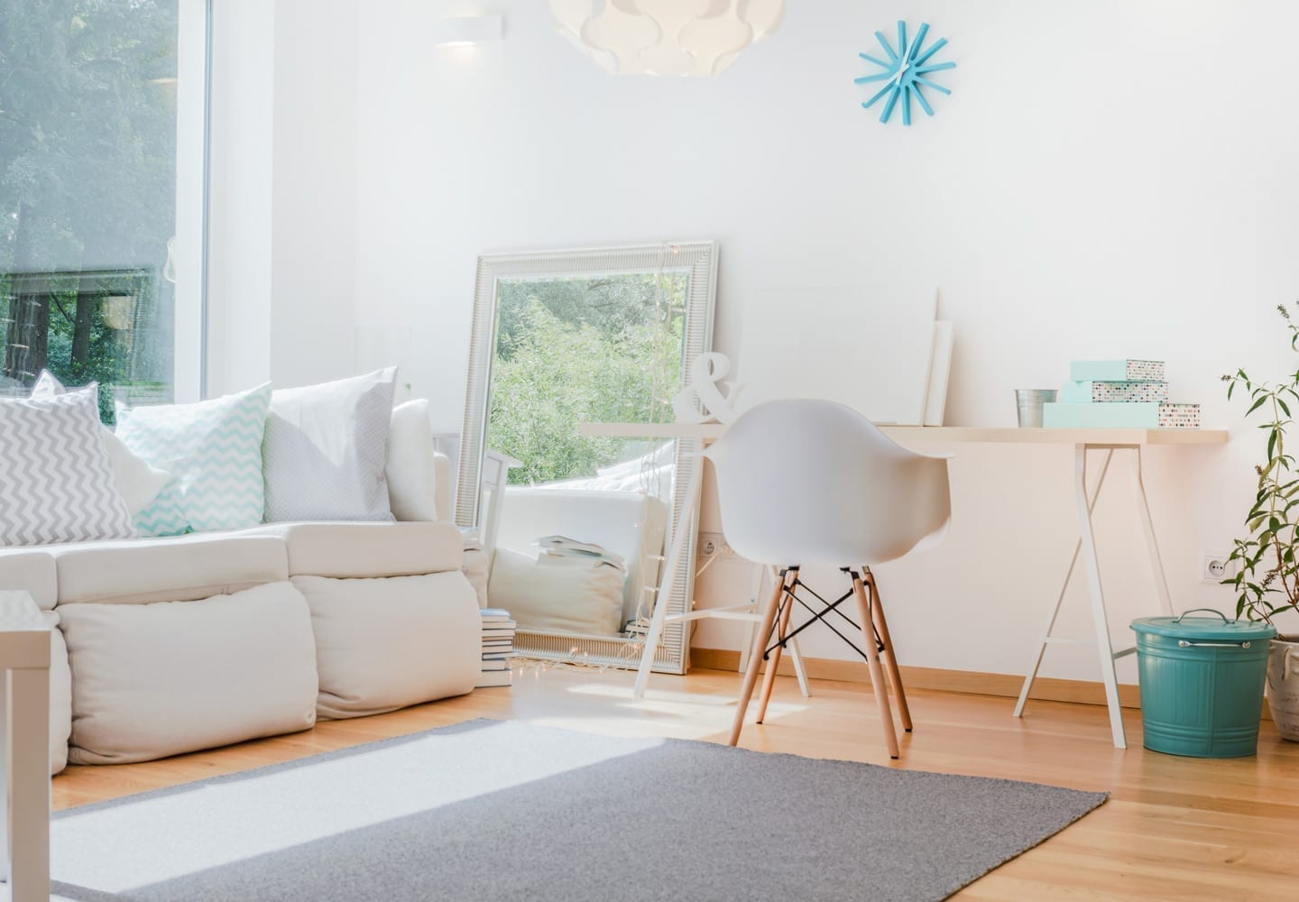 A small living room with light-colored furniture and a large mirror leaning against the wall.