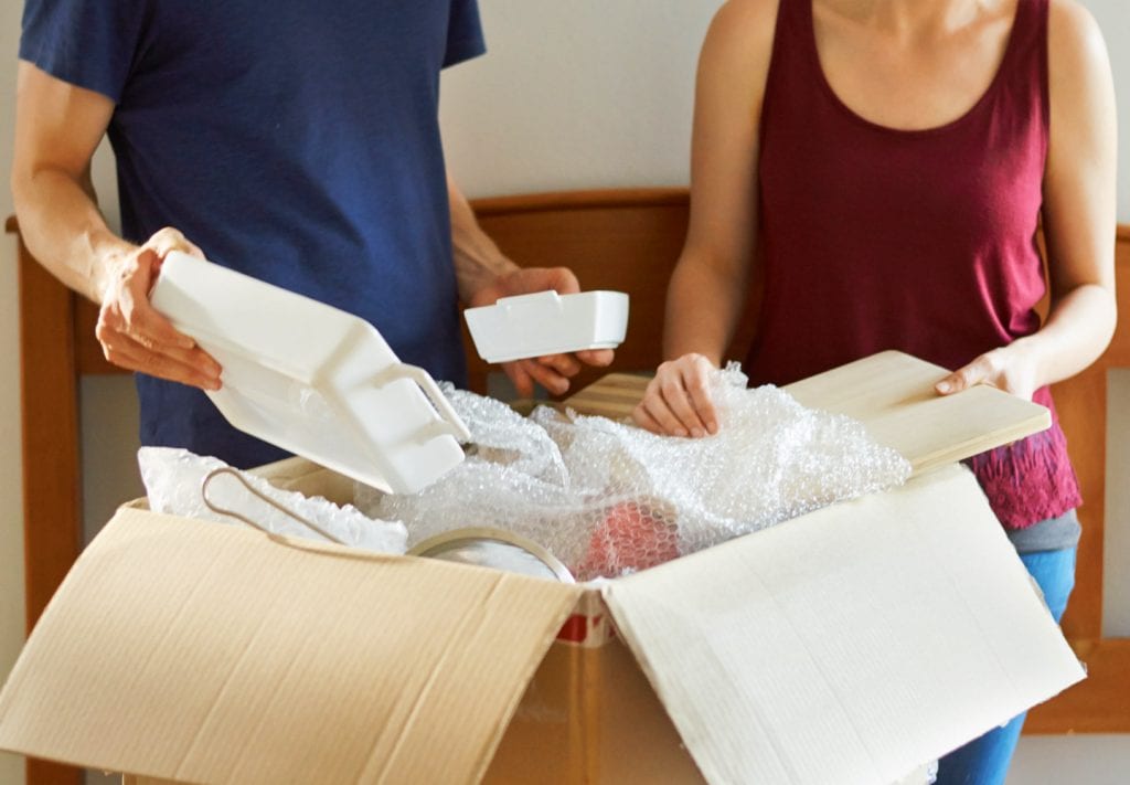 A man and woman packing baking dishes in a box with bubble cushioning roll