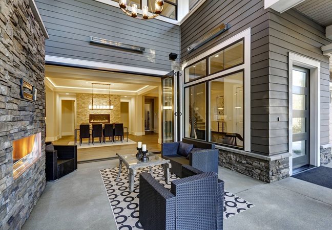 A recently refurbished patio living space. There is stone fireplace and black wicker chairs to sit on. 