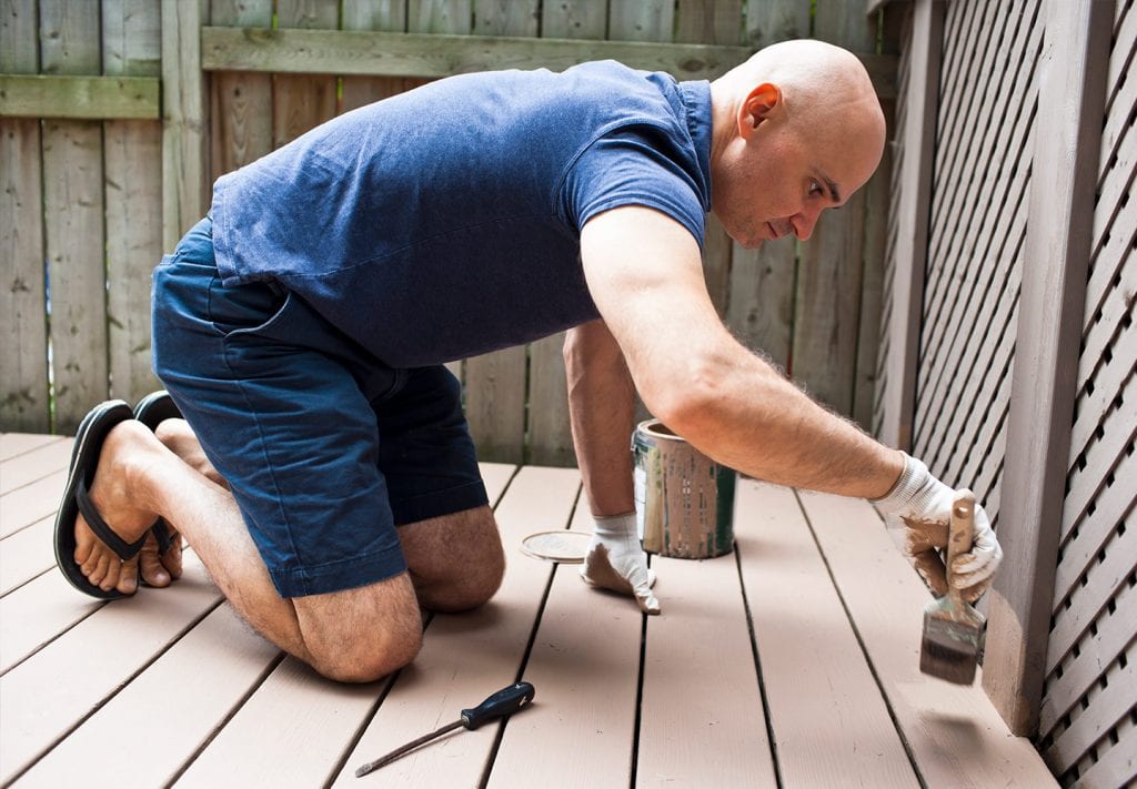 man painting a deck to prepare it for summer