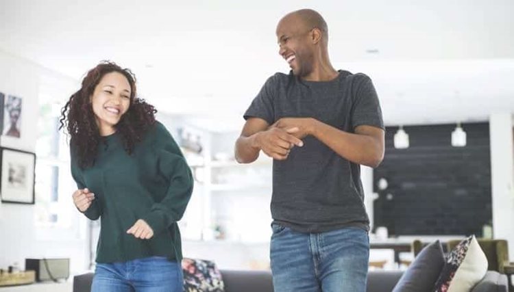 A man and woman are happily laughing and dancing together in their living room.