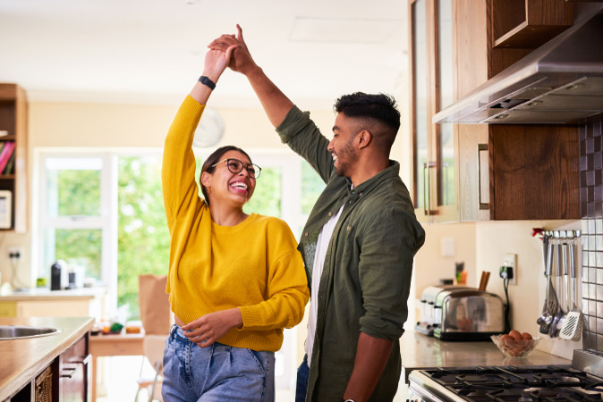 A couple is happily laughing and dancing in their kitchen after moving in together, showing that moving in with a boyfriend or moving in with a girlfriend can mean sharing lots of fun times.