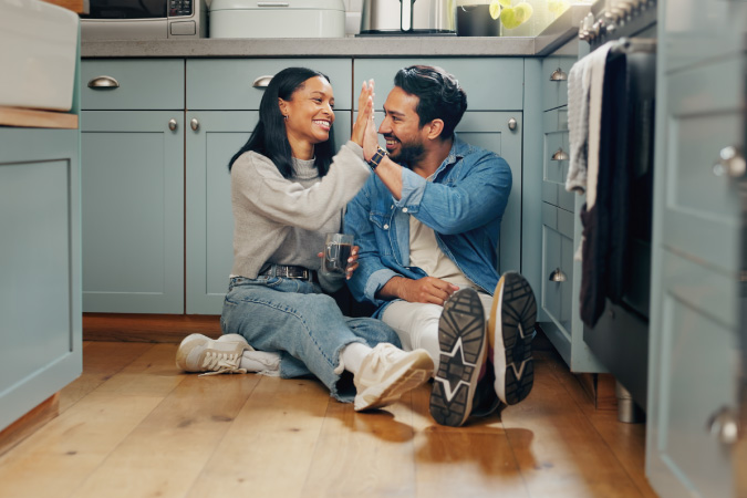 A happy couple, sitting on the kitchen floor, high-fives after they decide on moving in together.