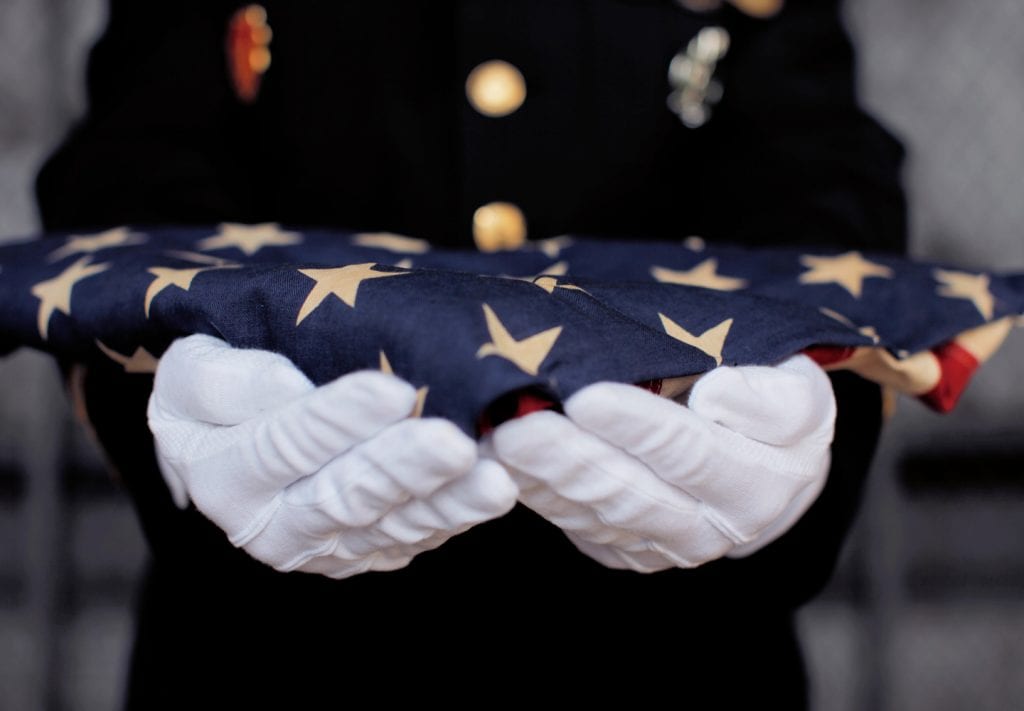 A uniformed solider holds a folded American flag
