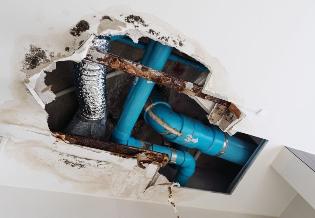 exposed pipes showing through a damaged apartment ceiling