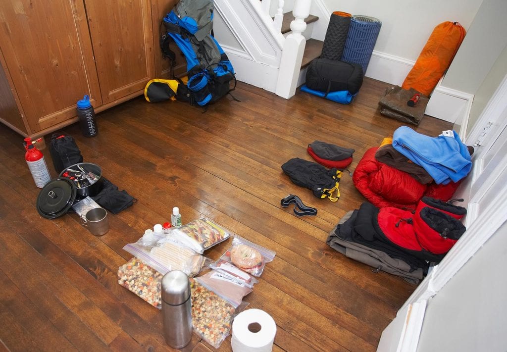 Neatly organized camping gear is organized by item on the floor of a home.