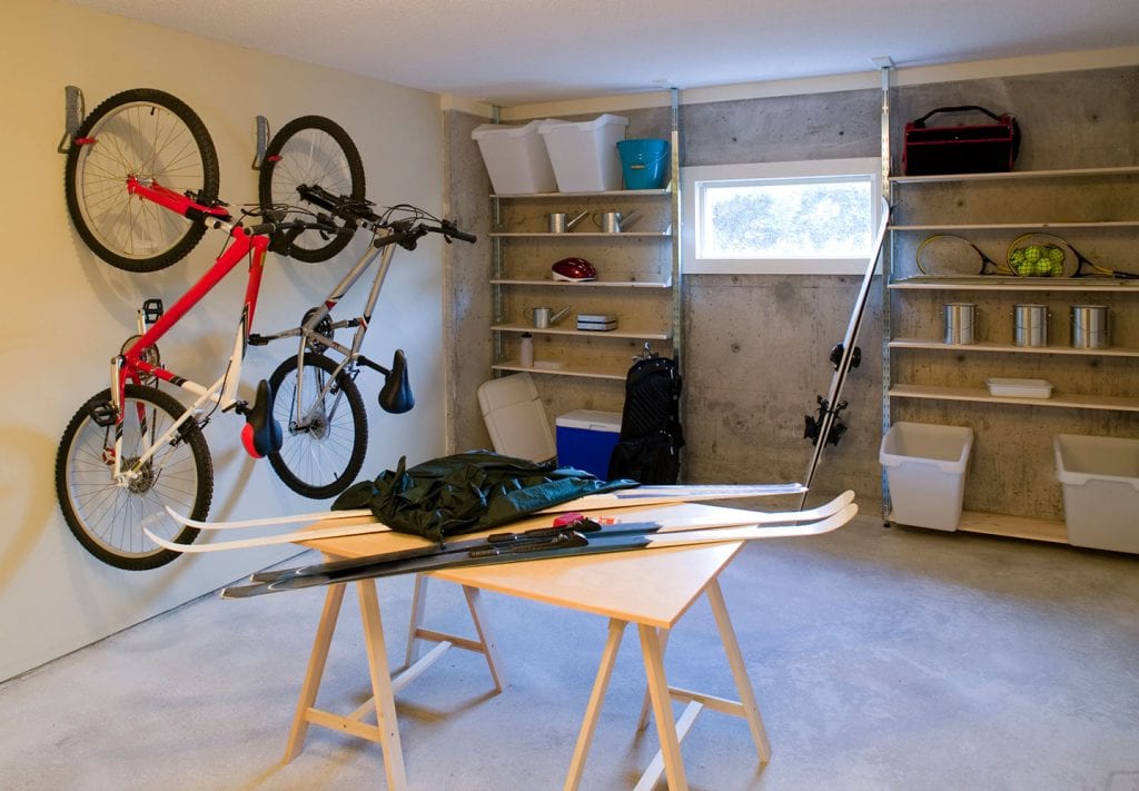 A garage neatly organized. There are two bikes hanging on the wall and there are skis on the floor. There are also shelves that have things neatly organized on them. 