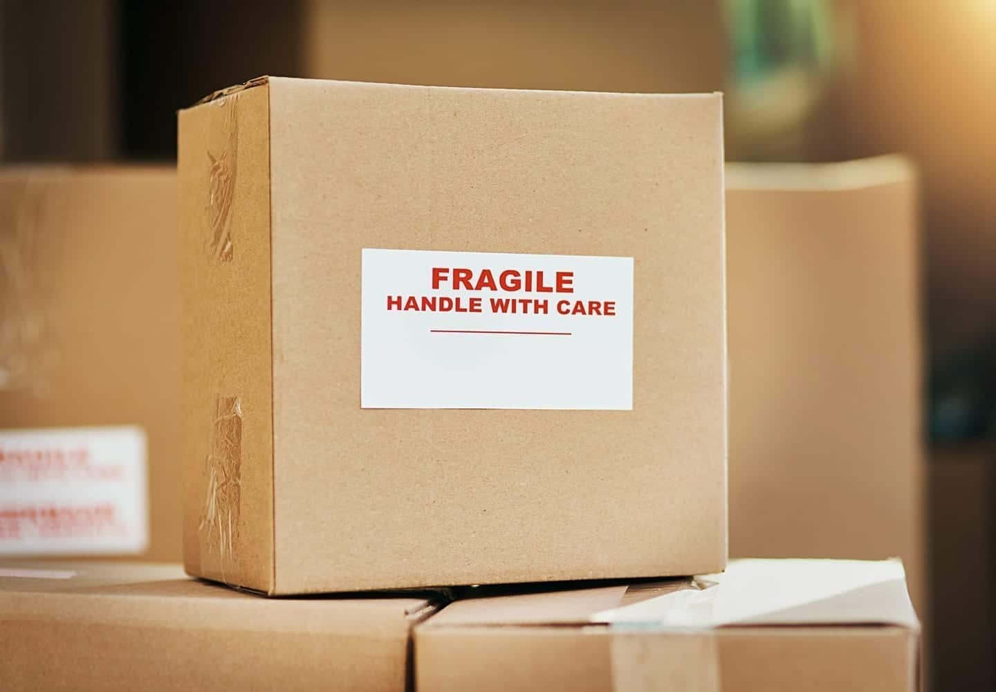 A moving box labeled, "FRAGILE, HANDLE WITH CARE" and stacked atop other moving boxes.