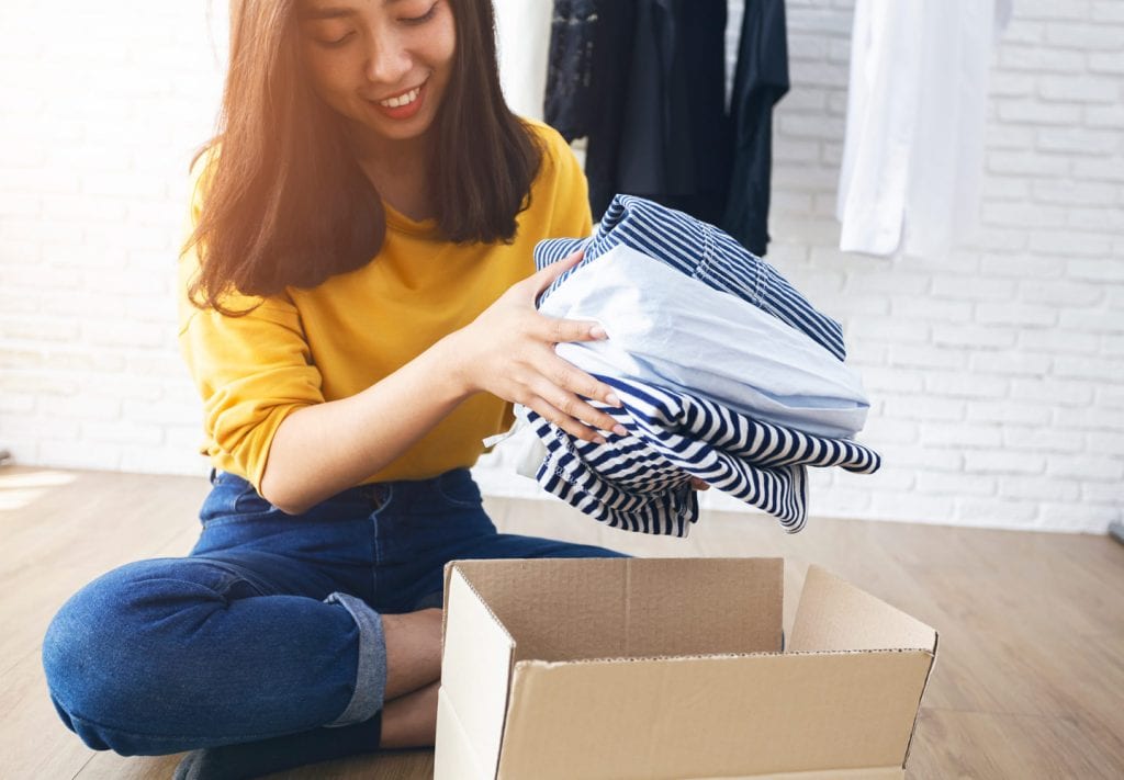 A young girl is packing seasonal clothes in a cardboard box for storage.