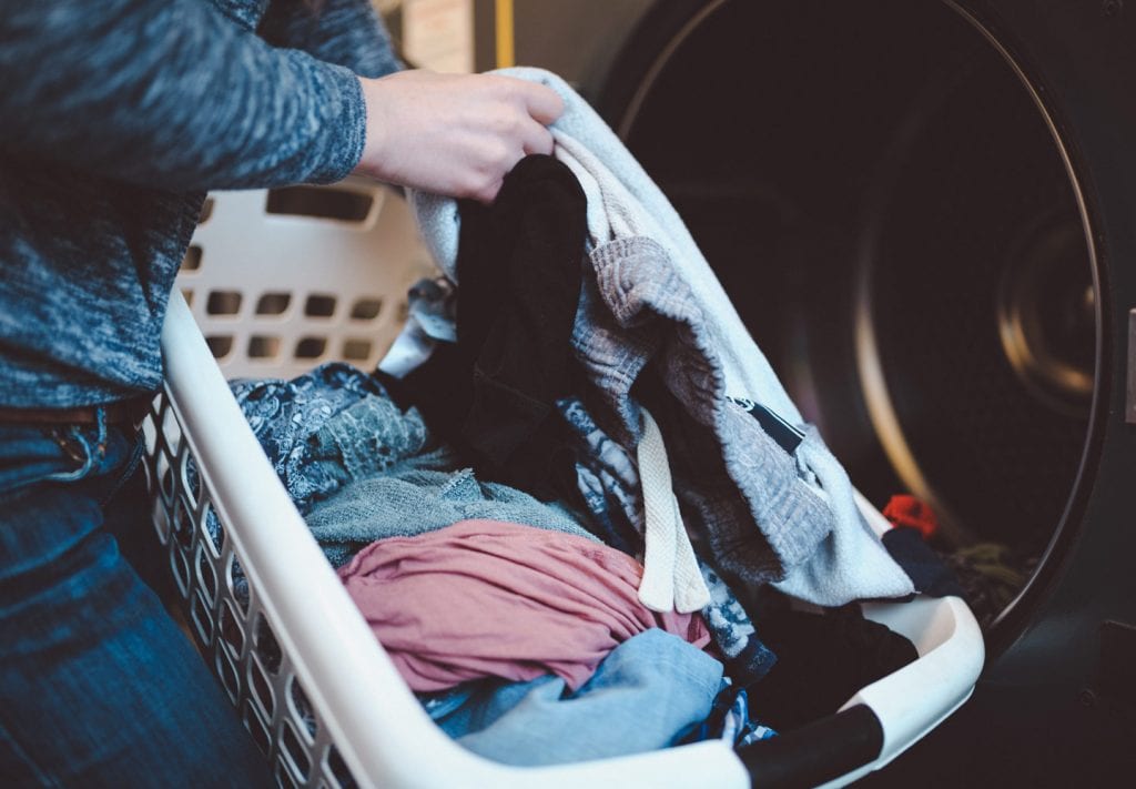 A woman is loading clothing into a washing machine to clean it before storing it.