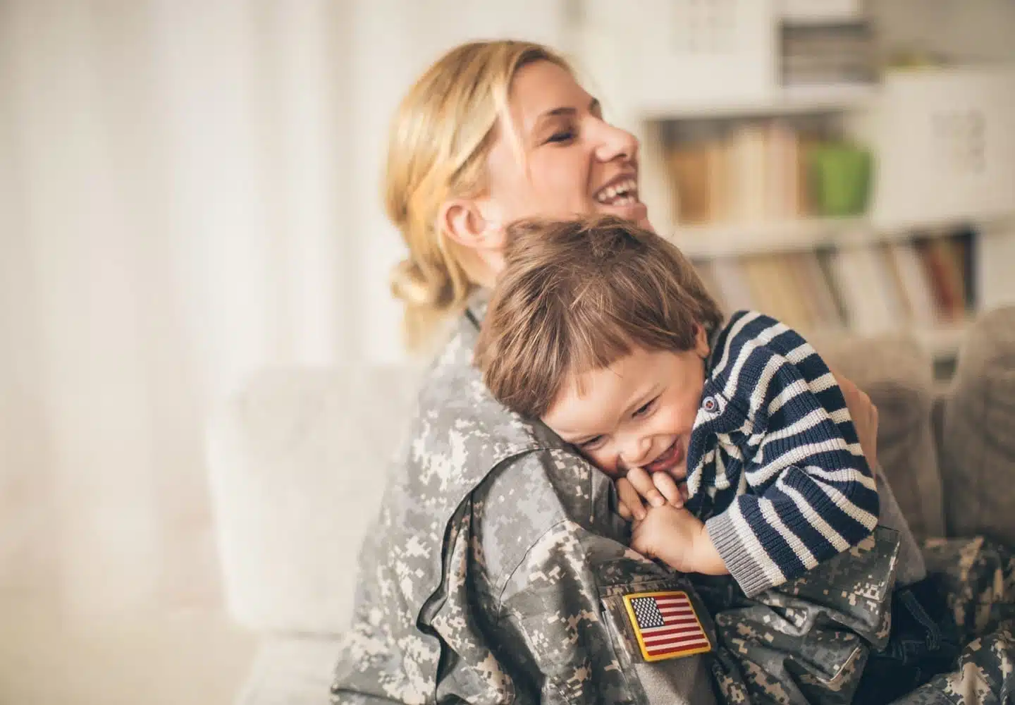 A woman in her military's uniform smiles as she hugs her young son.
