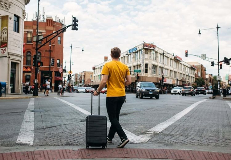 A traveler in a yellow T-shirt pulls a suitcase through a crosswalk