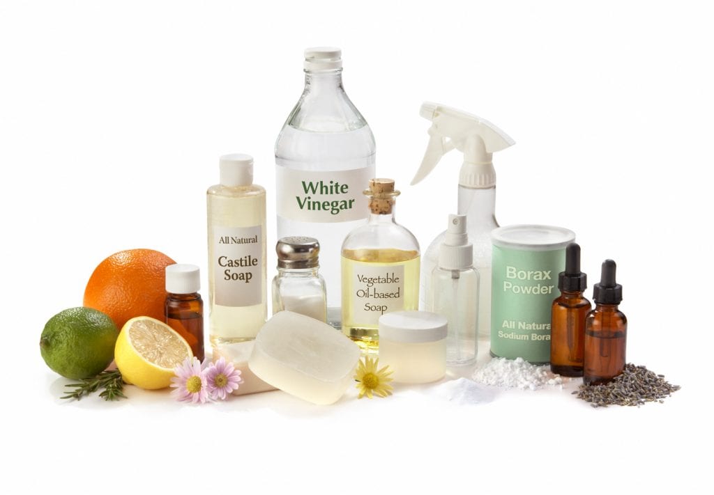 bottles of all natural cleaning prodcuts such as castile soap. white vinegar, and borax powder. There are also citrus fruits in the image. 