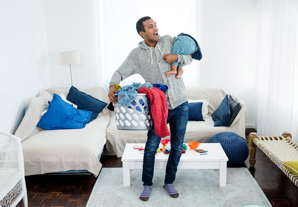 A father plays with son, slinging him over his shoulder as he holds a full laundry basket in his other hand