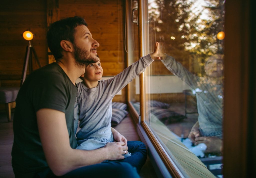 A man and his young son look out their window at a snowy winter scene.