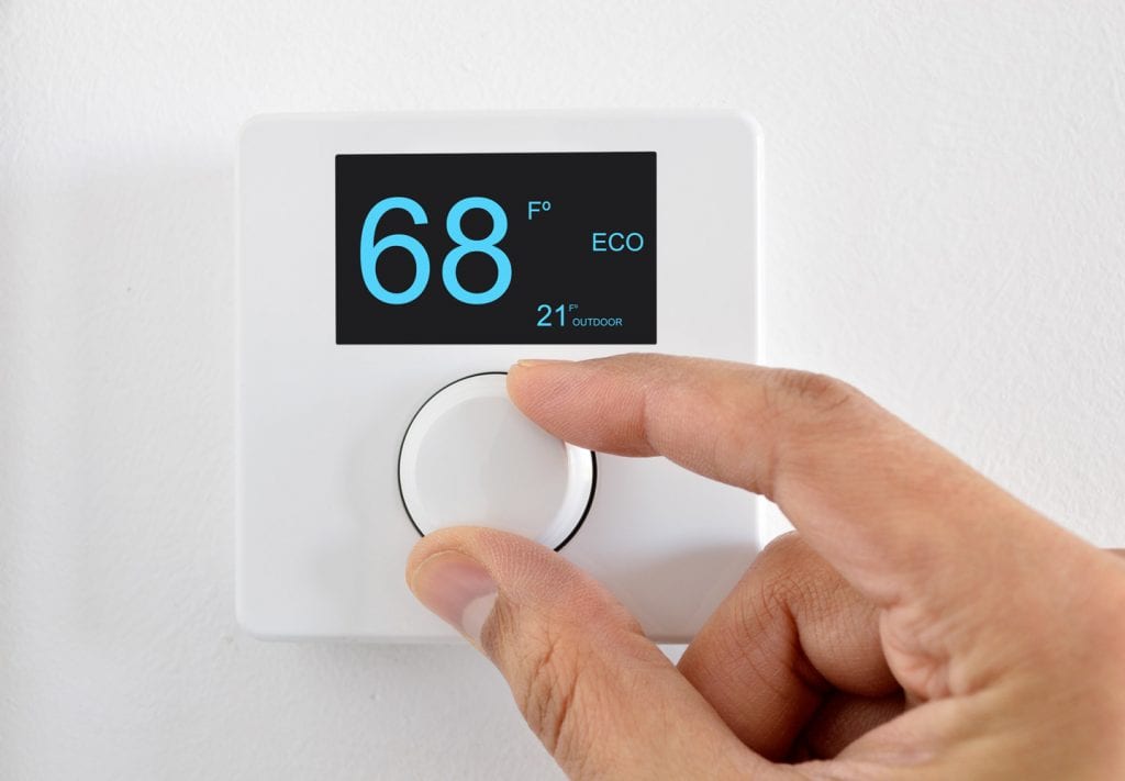 Fingers turning the dial on a thermostat. The temperature reads 68 F inside and 21 F outside.
