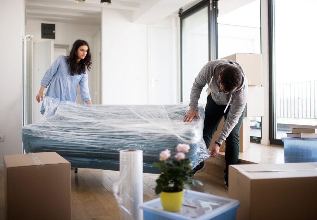 a couple wraps their furniture and packs boxes to place in climate-controlled storage