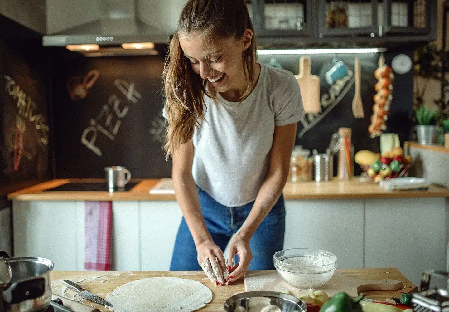 A young woman kneads pizza dough in her small kitchen. She's maximized her space by hanging common utensils and by keeping things uncluttered
