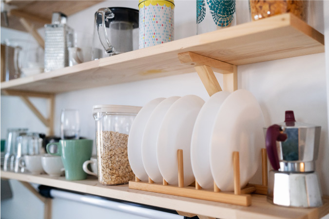 Close-up of some DIY wooden shelves that were recently installed in a small kitchen. The shelves are already neatly filled with cups, mugs, plates, and other kitchen items.