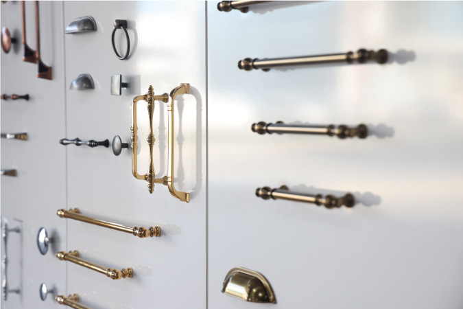 A white display wall has various cabinet pulls installed horizontally and vertically,  so customers can see what they might look like on their own cabinets.