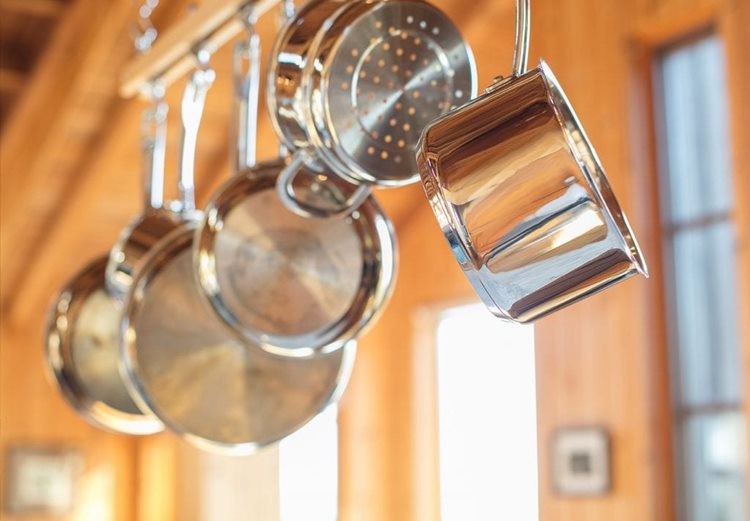 Stainless steel pots and pans are hanging from a suspended rack, maximizing the limited storage available in the small kitchen.