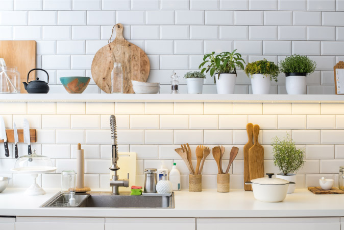 Various day-to-day cooking implements are arranged neatly on a kitchen counter and on the floating shelf above.
