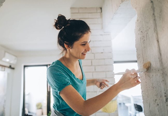 A young woman in a blue top paints columns in her home