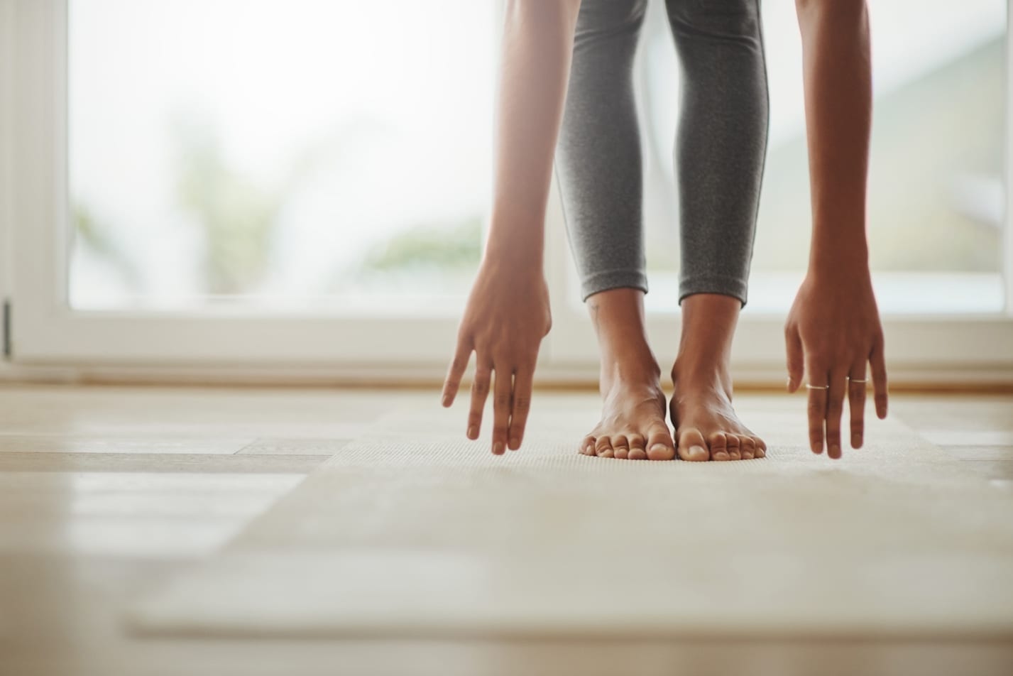 A close up of a woman in grey yoga pants grounds herself by touching the carpet. She also has a tattoo on her foot. 