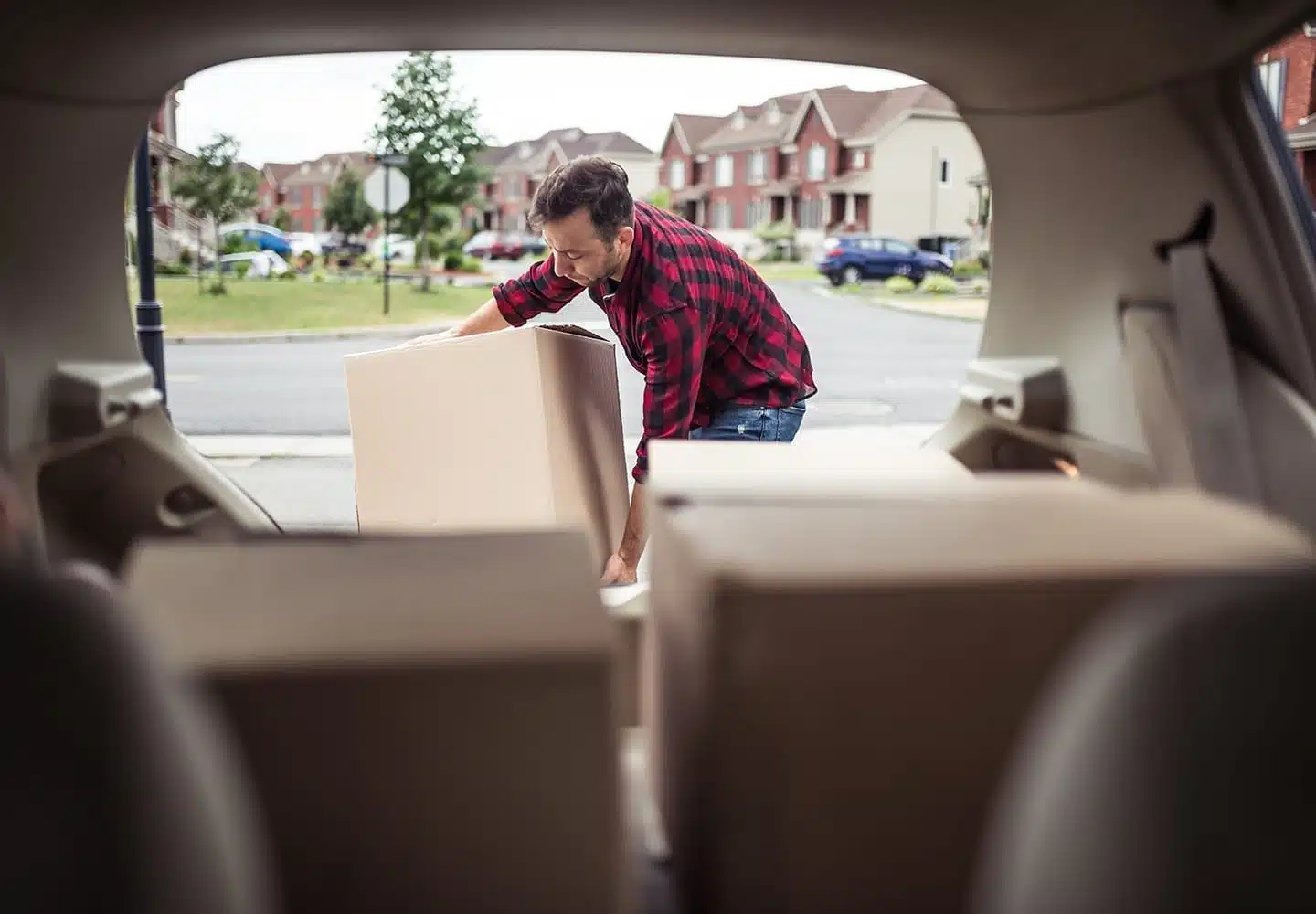 A man dressed in flannel loading boxes into the back of a car